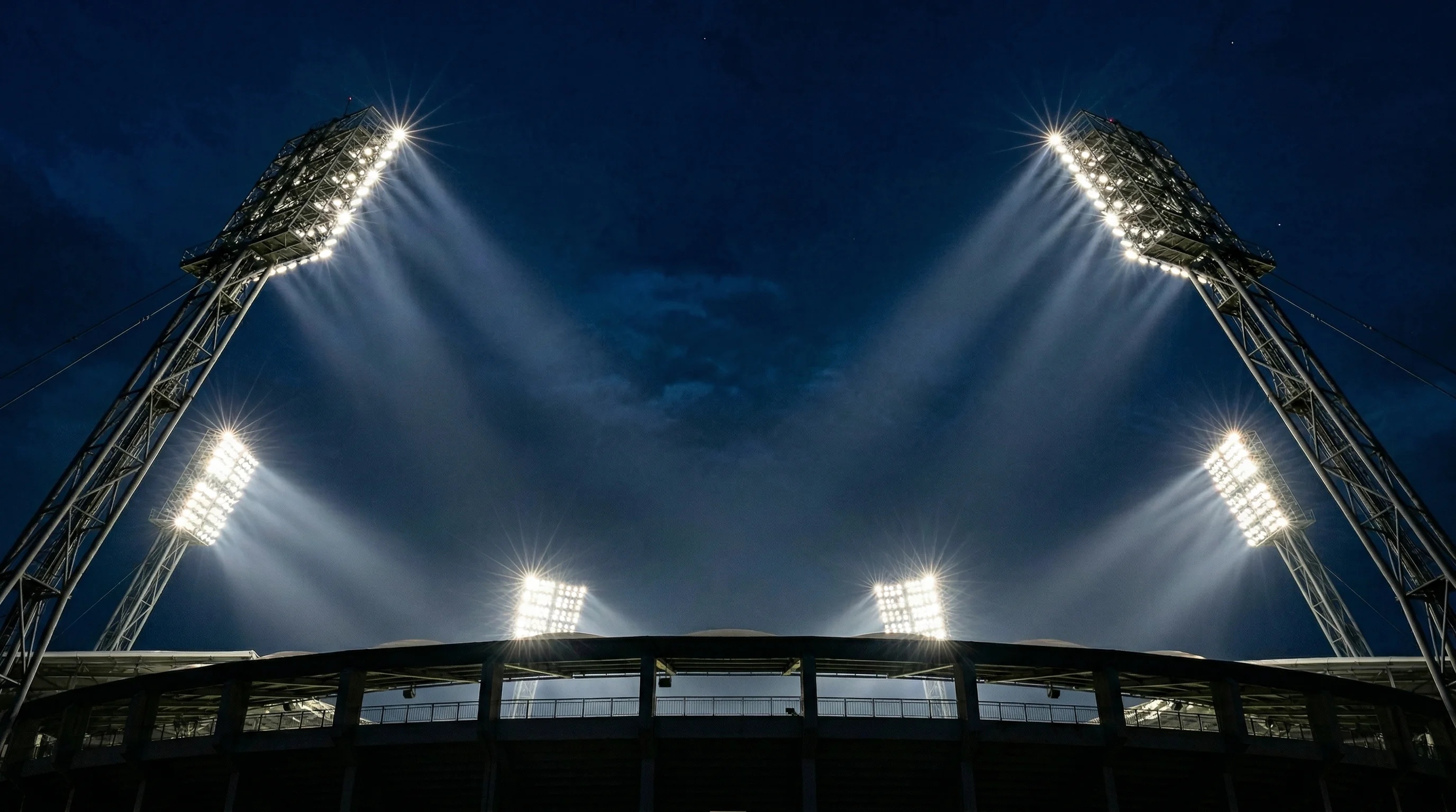 Flutlichtmasten eines großen Fußballstadions leuchten in den Nachthimmel vor einem europäischen Spiel