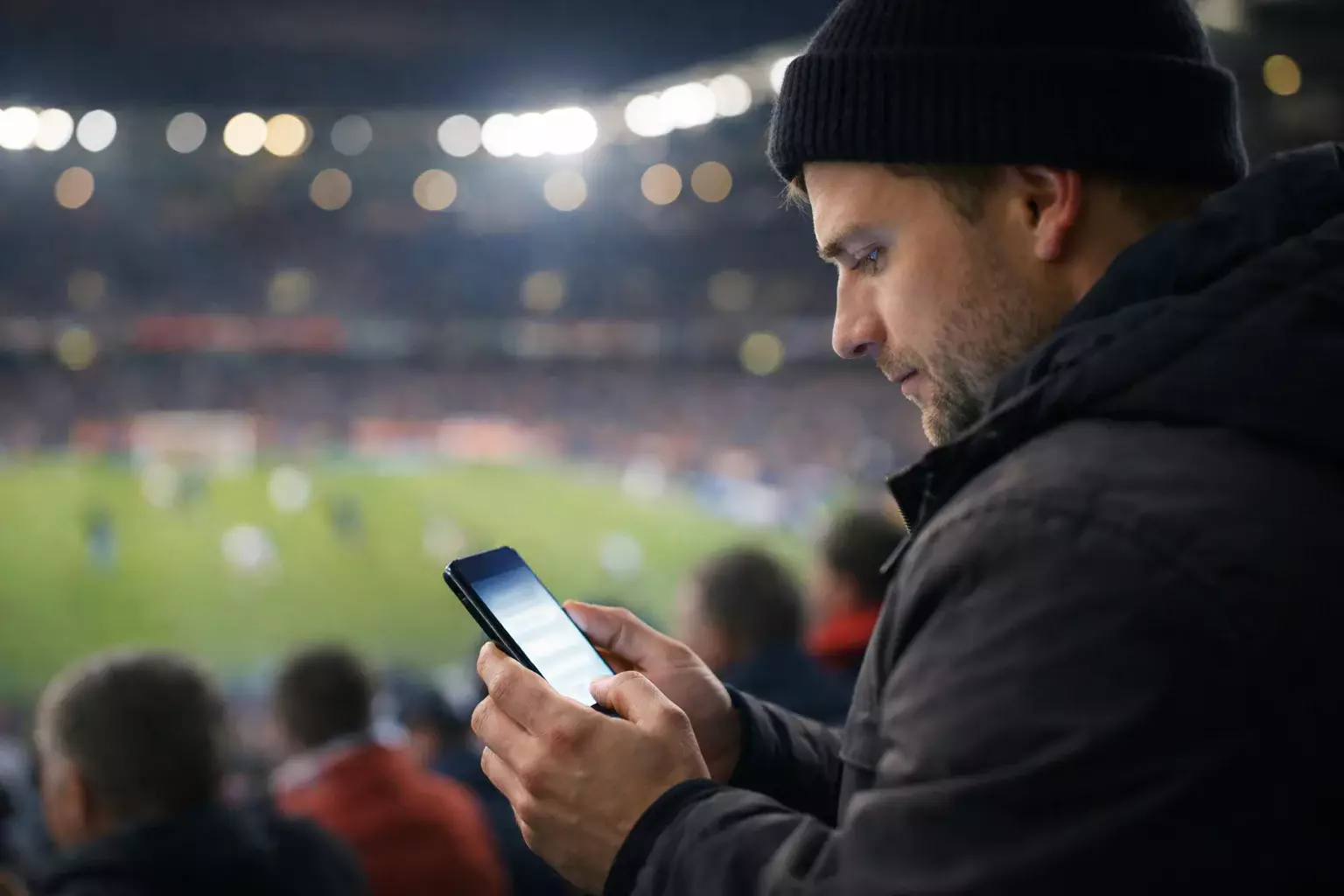 Fan schaut Fußballspiel im Stadion mit Smartphone in der Hand